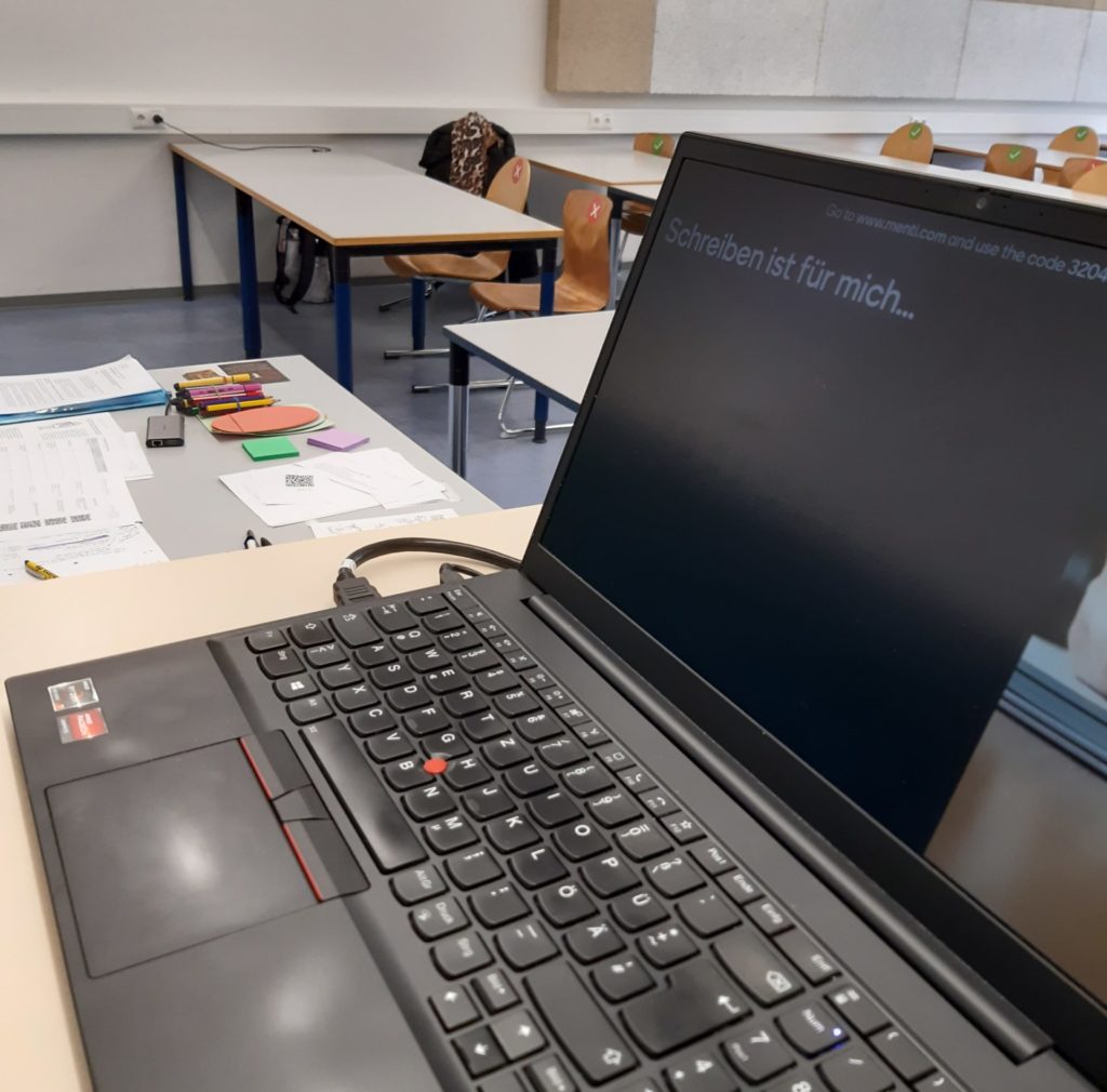 Ein Laptop mit Tastatur, im Hintergrund Stifte, Moderationskärtchen, Post-It-Notes